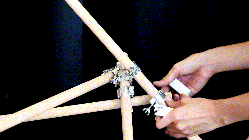 Hands manually aligning and fastening several tubes with conventional scaffold clamps